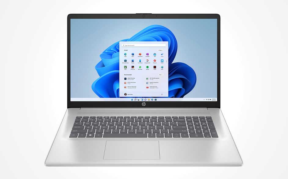 A silver laptop on white, showing a blue wave wallpaper and the Windows Start menu; full keyboard and a large touchpad, seen straight on.