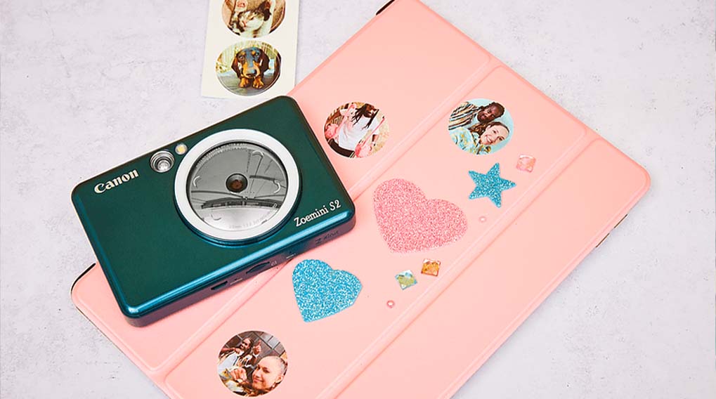 Groene Canon Zoemini S2 camera op een roze tablet met stickers en glittervormen. Stickervel met dieren linksboven.