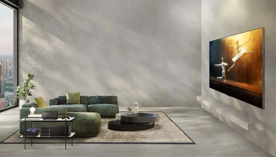 Een woonkamer met groene bank, ronde tafel op een vloerkleed en een tv met een afbeelding van dansers.