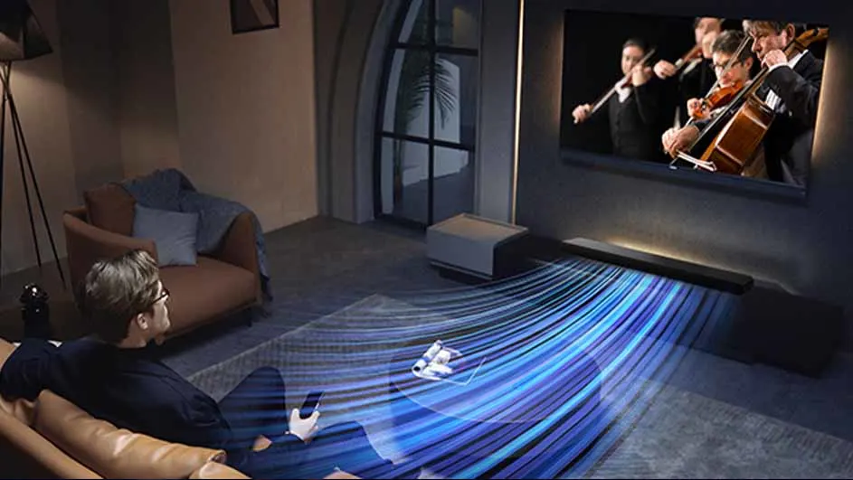 Man zit op een bank met een afstandsbediening, kijkend naar een tv met een orkest. Een soundbar staat onder de tv.