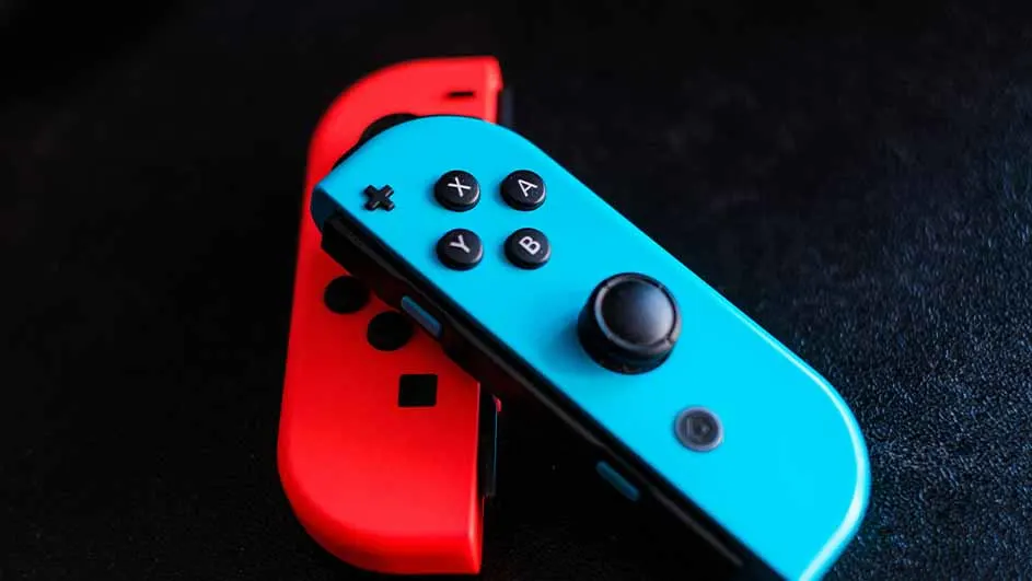 Twee Nintendo Switch Joy-Con controllers, één rood en één blauw, liggen op een zwarte achtergrond.