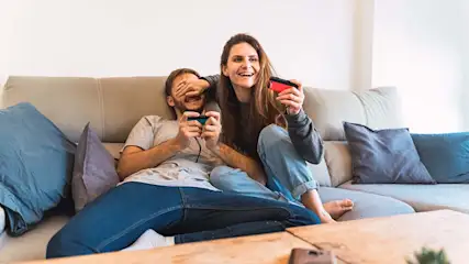 Op een bank zitten een man en een vrouw met controllers in hun handen, klaar om een spel te spelen.