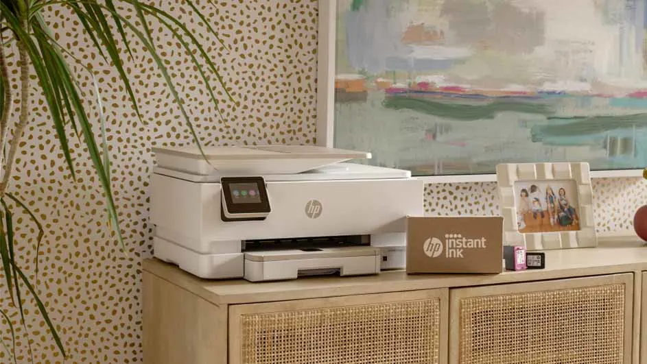 Een witte printer staat op een houten kast naast een plant, een schilderij en een fotolijst.
