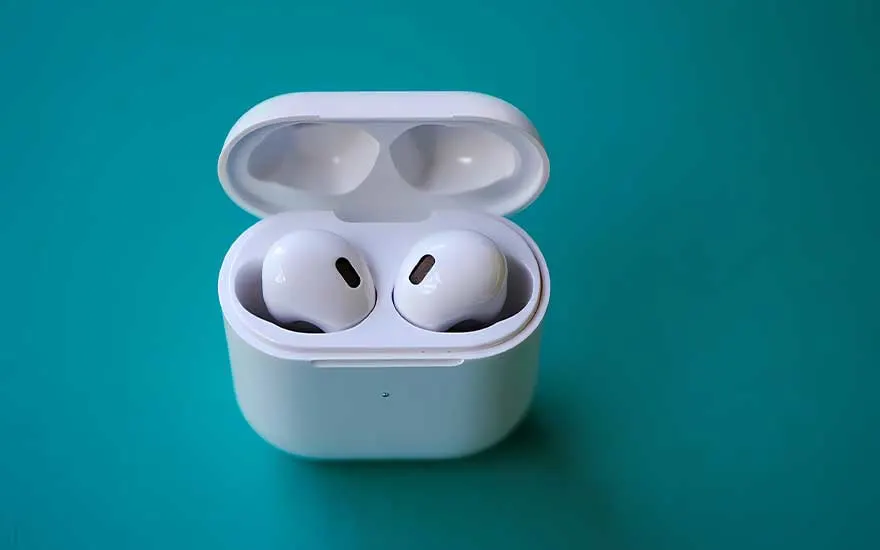 Een compacte witte oplaadcase ligt op een effen turquoise ondergrond, met twee draadloze oordopjes zichtbaar in de open doos.