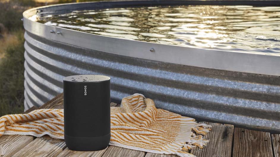 Een zwarte Sonos speaker staat naast een metalen badkuip op een houten platform, met een gestreepte handdoek.