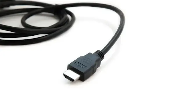 Een zwarte HDMI-kabel ligt op een witte ondergrond, met de connector duidelijk zichtbaar en het opschrift "HDMI" op de stekker.