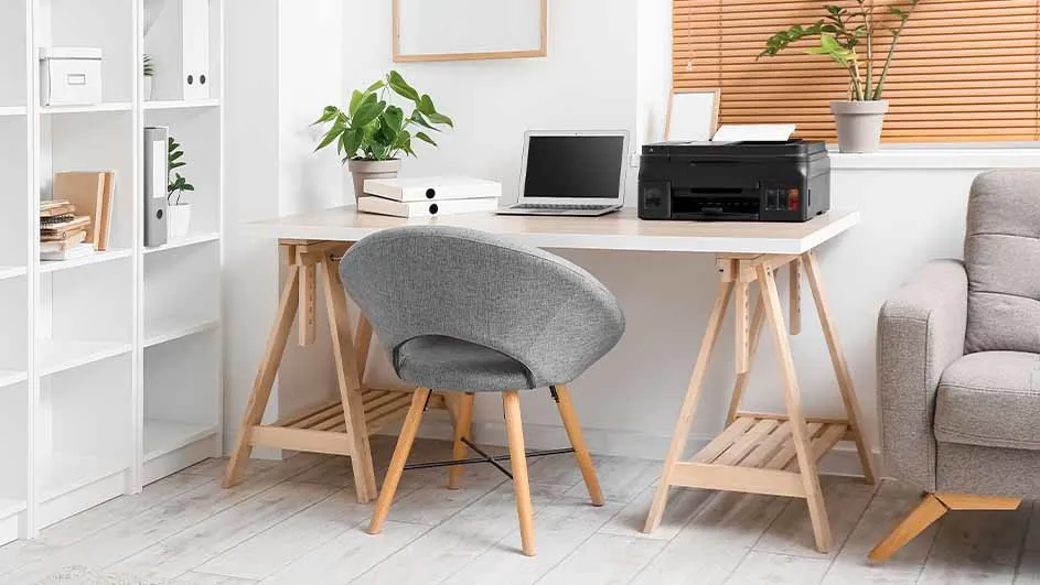 Kantoorruimte met een houten bureau, grijze stoel, printer, laptop, boeken, plant en een witte boekenkast.