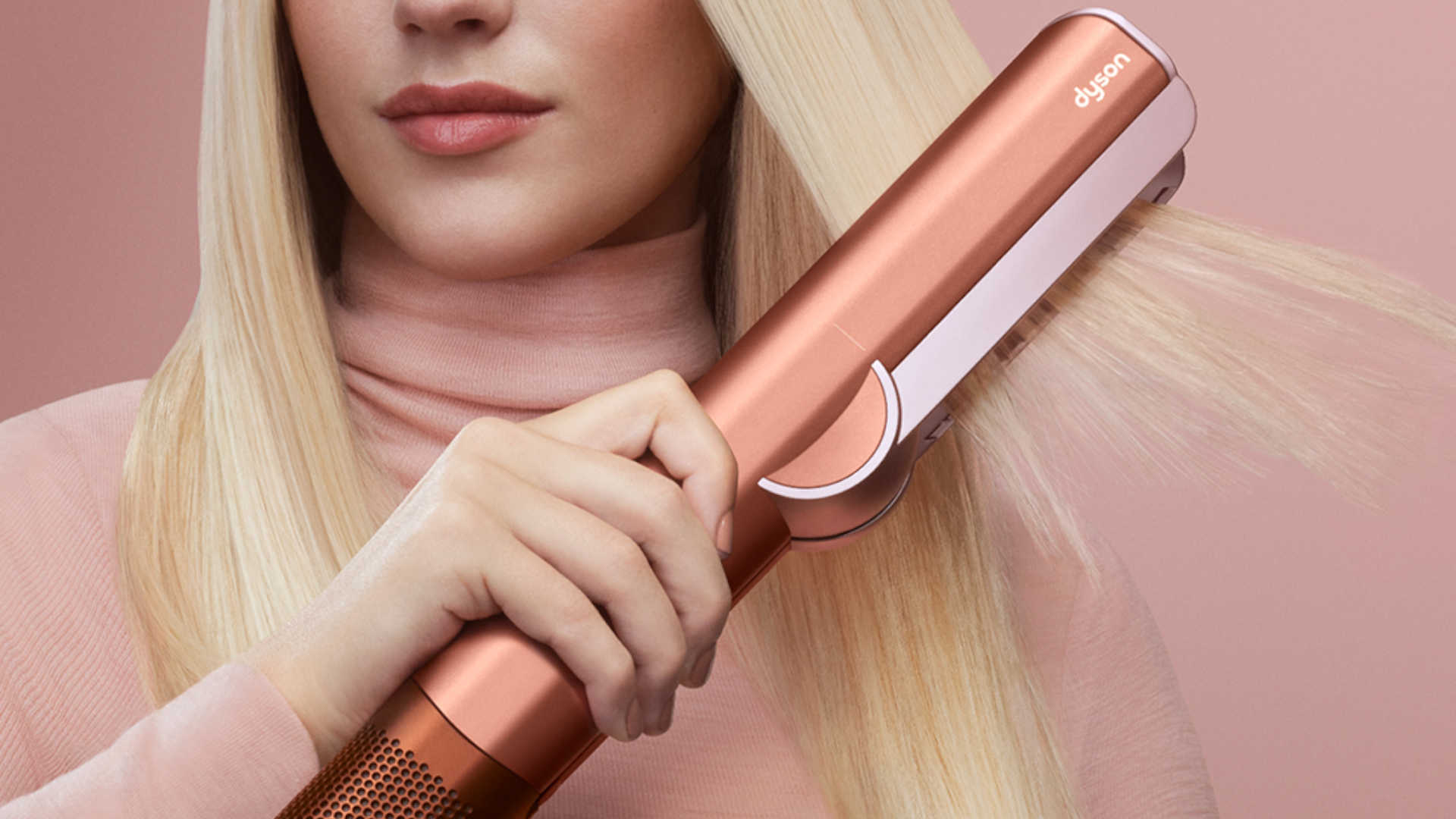 Persoon gebruikt een roségouden stijltang om lang, steil blond haar te stylen tegen een roze achtergrond.