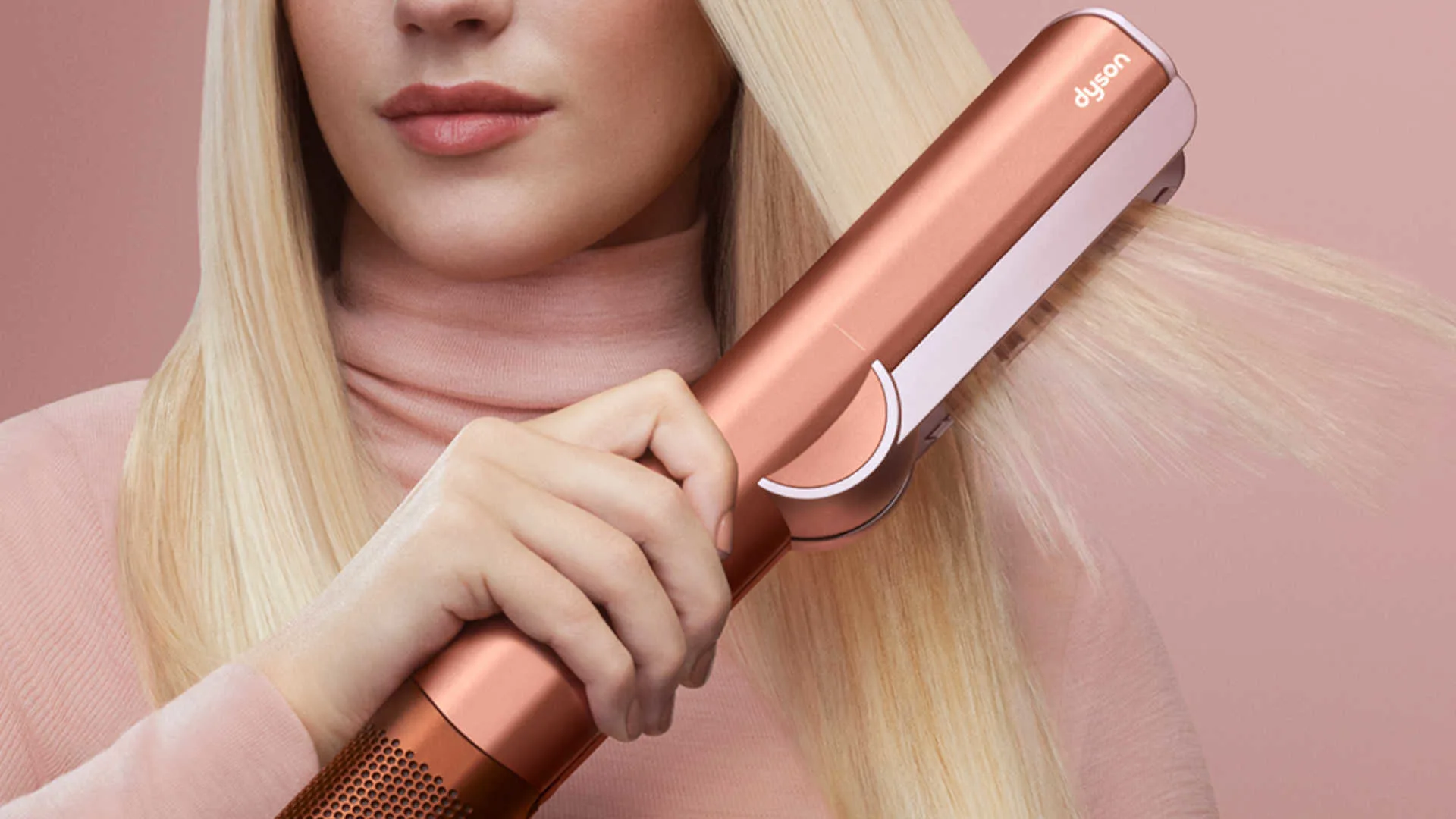 Persoon gebruikt een roségouden stijltang om lang, steil blond haar te stylen tegen een roze achtergrond.