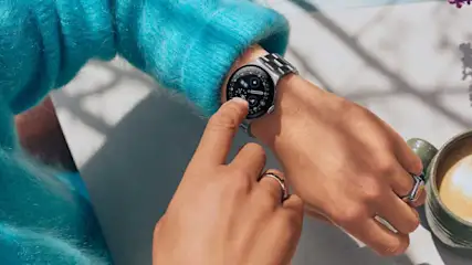 Een smartwatch met metalen band wordt bediend met aanraking op het scherm, naast een kop koffie.