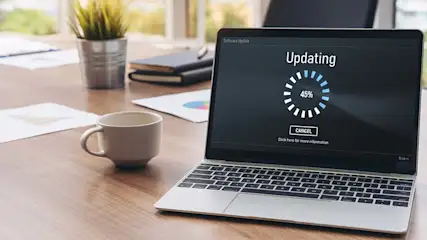 Laptop toont "Updating" met 45% voltooid, mok, plant en documenten op een houten bureau.