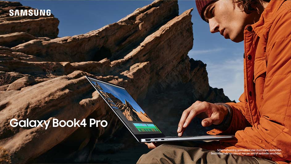 Een persoon met oranje jas gebruikt een Samsung Galaxy Book4 Pro-laptop voor een rotsachtige achtergrond onder een blauwe hemel.