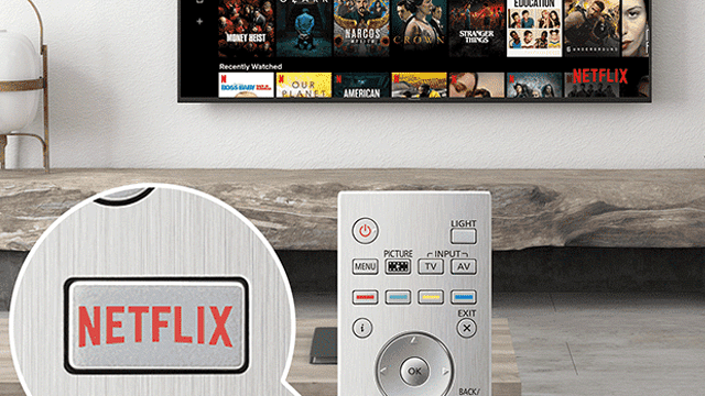 Een tv aan de muur toont een Netflix-menu. Een afstandsbediening en een Netflix-knop liggen op een houten oppervlak.