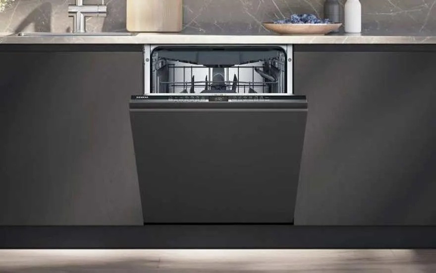 Een Siemens inbouwvaatwasser met een zwarte deur staat open in een moderne keuken met donkergrijze kasten en een licht aanrechtblad.