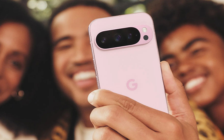 Roze Google Pixel smartphone wordt vastgehouden tijdens groepsfoto. Vrienden lachen op achtergrond terwijl camera-eiland prominent zichtbaar is.