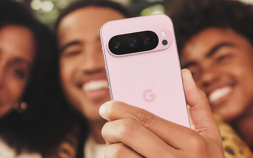 Roze Google Pixel smartphone wordt vastgehouden tijdens groepsfoto. Vrienden lachen op achtergrond terwijl camera-eiland prominent zichtbaar is.
