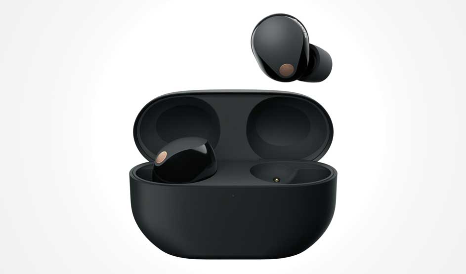 A black charging case sits open; one earbud rests inside and another hovers above, with small copper-toned details on a pale backdrop.