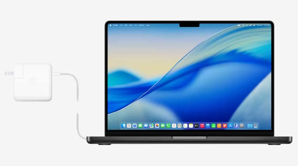 Close up of an open laptop displaying a bright blue wave wallpaper, connected to a white charger plugged in on the left side.