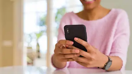 Close-up van een vrouw die binnen, in zacht daglicht, haar smartphone vasthoudt en met haar andere hand op het scherm tikt.