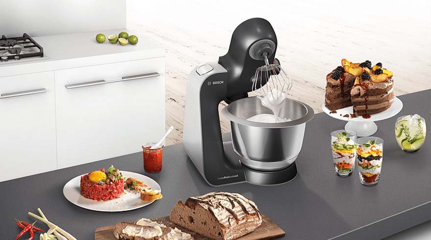 Een keukenopstelling met een Bosch keukenmachine, diverse gerechten zoals taart, steak tartaar en brood.