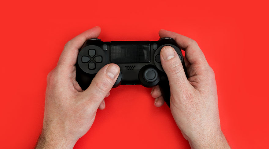 Twee handen houden een zwarte Playstation-controller vast tegen een rode achtergrond.