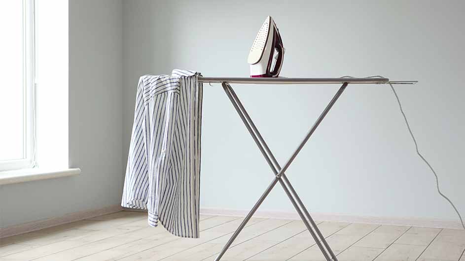 Strijkijzer op strijkplank met gestreept overhemd, in lichte kamer met houten vloer en raam.