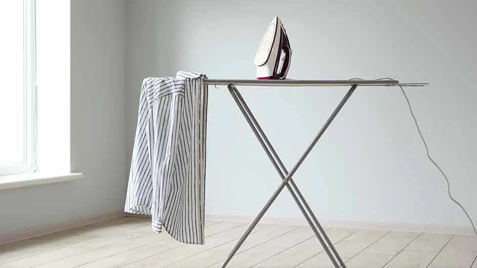 Strijkijzer op strijkplank met gestreept overhemd, in lichte kamer met houten vloer en raam.