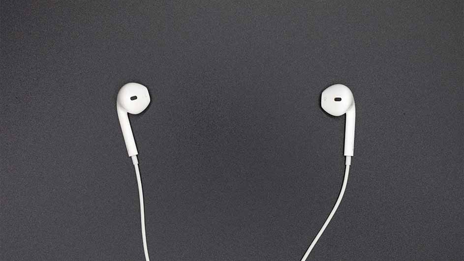 Twee witte oordopjes met snoer liggen op een donkergrijze achtergrond. Elk oordopje is apart te zien.