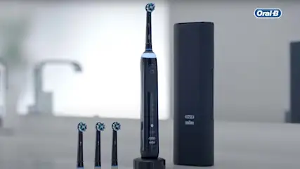 Een zwarte Oral-B elektrische tandenborstel staat naast een houder en drie opzetborstels op een grijze ondergrond.