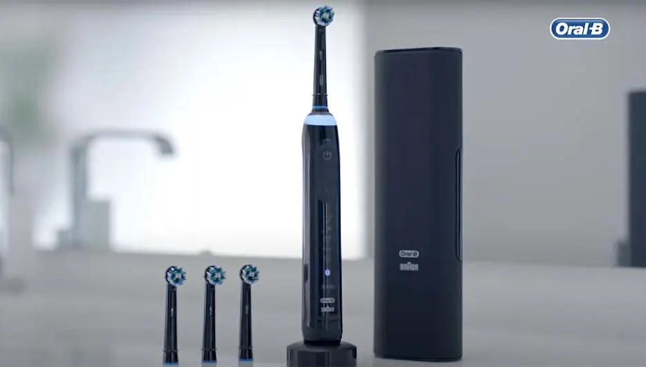 Een zwarte Oral-B elektrische tandenborstel staat naast een houder en drie opzetborstels op een grijze ondergrond.