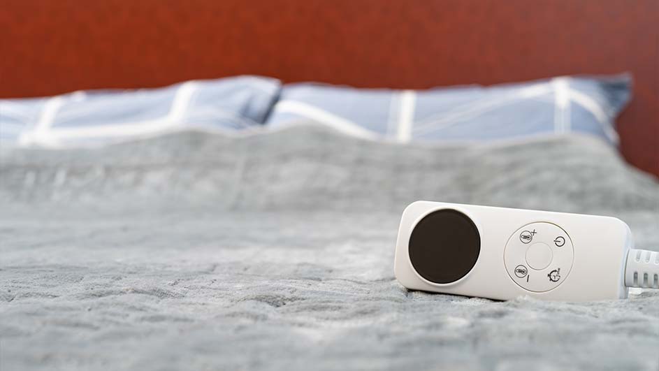 Een wit bed met blauwe kussens en een rode achterwand. Een witte bedieningseenheid met een ronde, zwarte knop ligt op het bed.