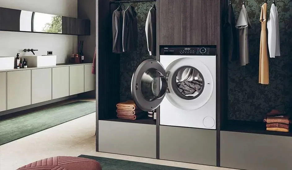 Stijlvolle wasruimte met ingebouwde wasmachine in een kast, deur open, omringd door hangende kleding en netjes opgevouwen handdoeken