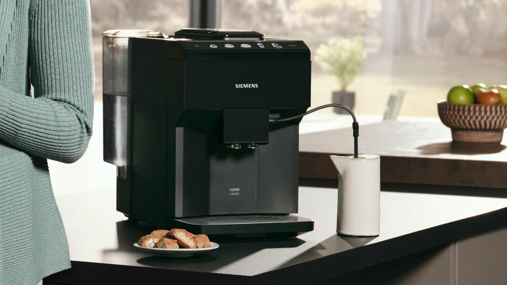 Een zwarte Siemens EQ500 koffiemachine staat op een aanrecht, naast een wit kannetje en een bord met koekjes.