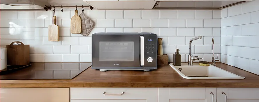 A kitchen scene shows a microwave, sink, and faucet on a wooden countertop with white cabinets and tiled walls.