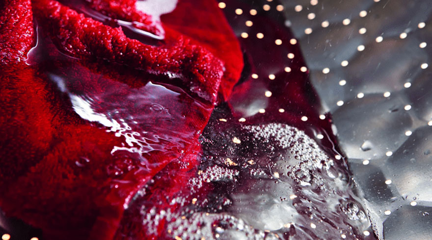 Rode stof in water met bubbels, tegen een zilverkleurige geperforeerde achtergrond.