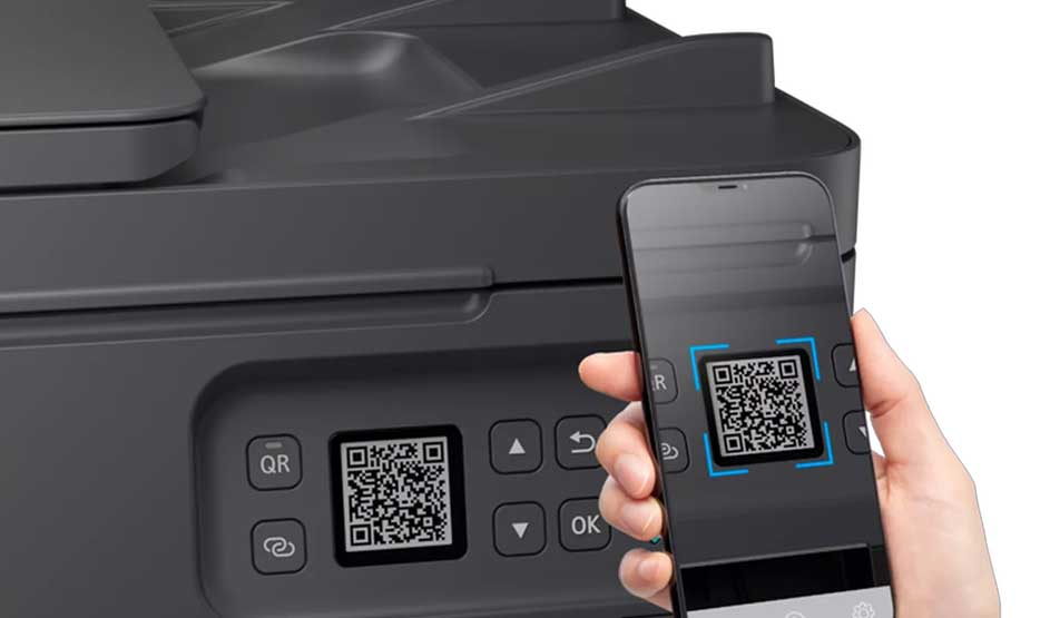 Een hand scant een QR-code op het bedieningspaneel van een zwarte Canon printer met een smartphone. Het Canon-logo is niet zichtbaar.