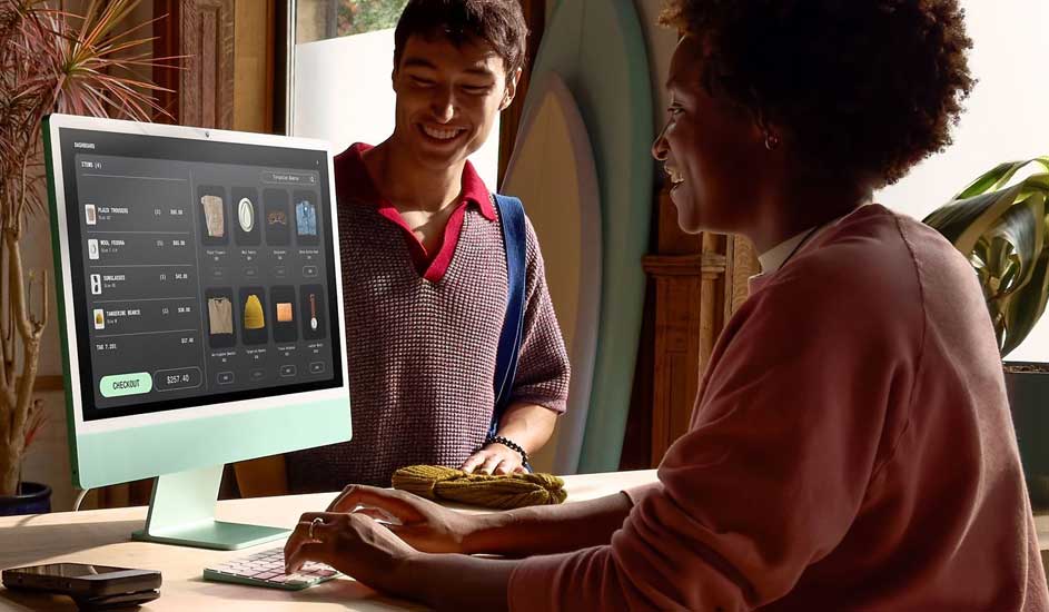 Op de afbeelding rekent iemand kleding af op een groene Apple iMac bij een toonbank, met surfplanken en planten op de achtergrond.