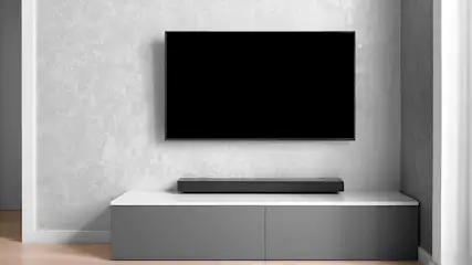 Zwarte tv aan de muur boven wit en grijze kast met een zwarte soundbar erop in een kamer.