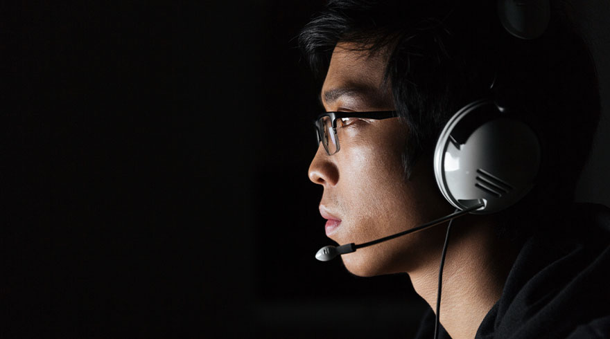 Een man met een bril en een witte headset met microfoon kijkt naar links tegen een donkere achtergrond.