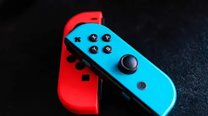 Twee Nintendo Switch Joy-Con controllers, één rood en één blauw, liggen op een zwarte achtergrond. De blauwe controller ligt bovenop de rode.