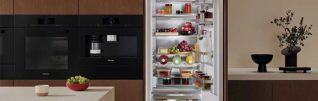 Een moderne keuken met Miele inbouwapparatuur en een goed gevulde koelkast. Boven de koelkast staan voorraadpotten met pasta. De houten kasten geven een warme uitstraling.