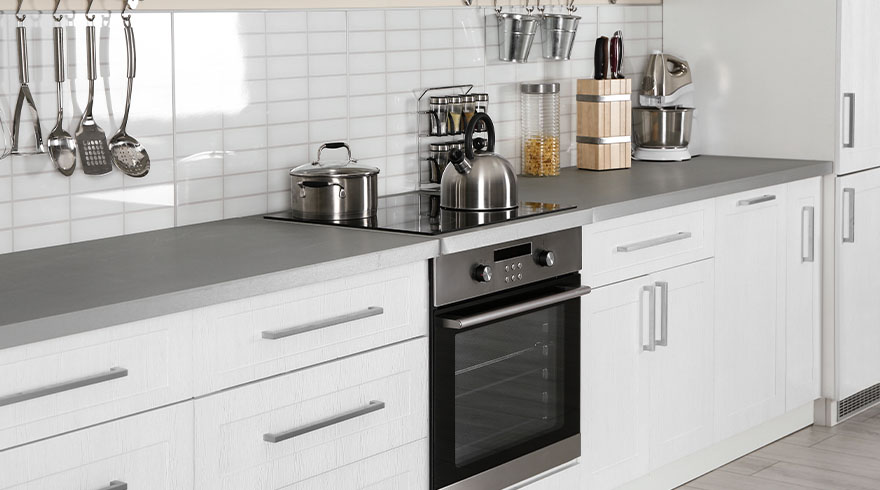 Een keuken met witte kasten, een grijs aanrechtblad en diverse kookgerei, waaronder een waterkoker en een pan op een kookplaat.