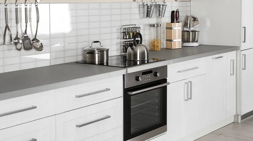 Een keuken met witte kasten, een grijs aanrechtblad en diverse kookgerei, waaronder een waterkoker en een pan op een kookplaat.