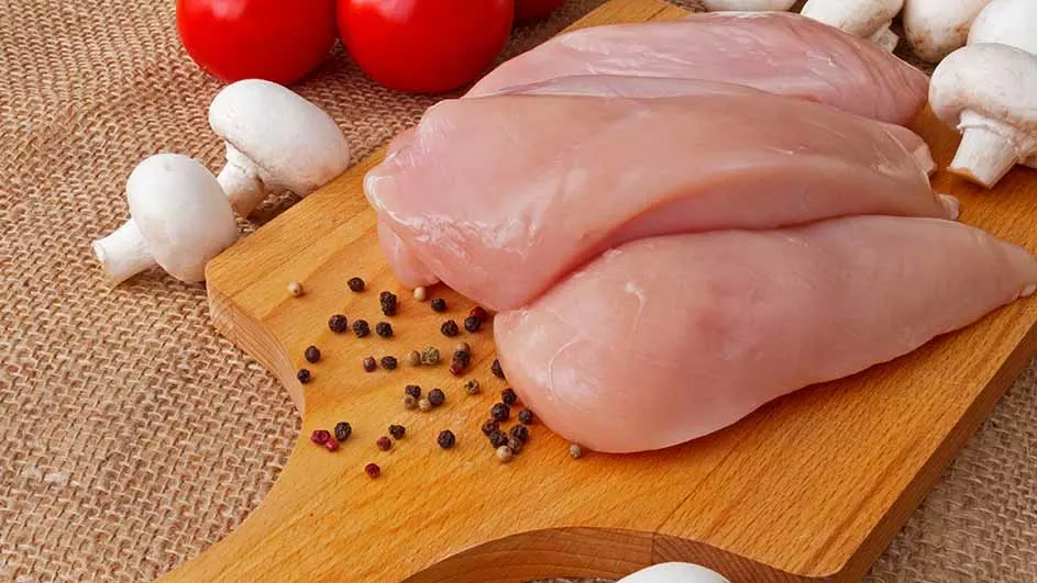 Kippenvlees, champignons, tomaten en peperkorrels op een houten plank. De plank ligt op een jute achtergrond.
