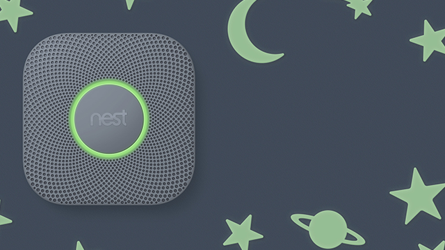 Grijze Nest-detector met groene ring op blauwe achtergrond met maan, sterren en planeet decoratie.