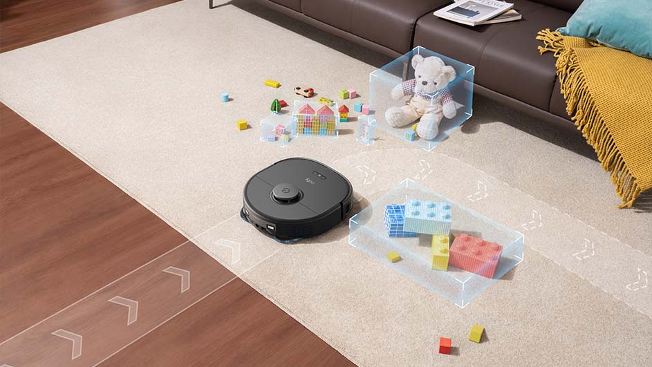 Een zwarte robotstofzuiger op een beige vloerkleed, omringd door speelgoed en blokken. Een bruine bank is gedeeltelijk zichtbaar op de achtergrond.