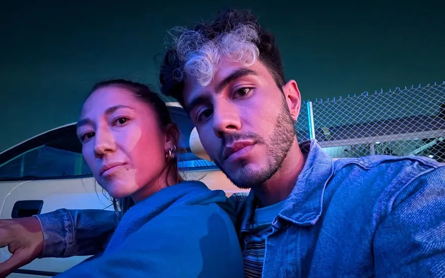 Twee personen maken een selfie in een auto met dramatische blauw-paarse verlichting. Moderne, sfeervolle nachtfoto met neonkleuren.