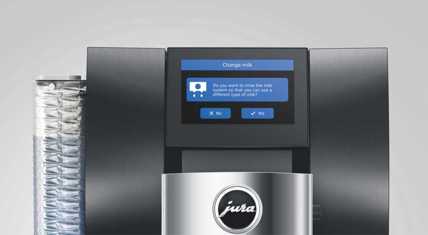 Close-up van een moderne Jura koffiemachine met touchscreen waarop een melding staat om het melksysteem te spoelen aan de voorkant.