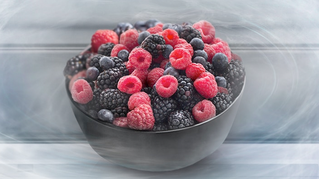 Een kom vol rood frambozen, blauwe bosbessen en zwarte bramen tegen een lichte achtergrond.