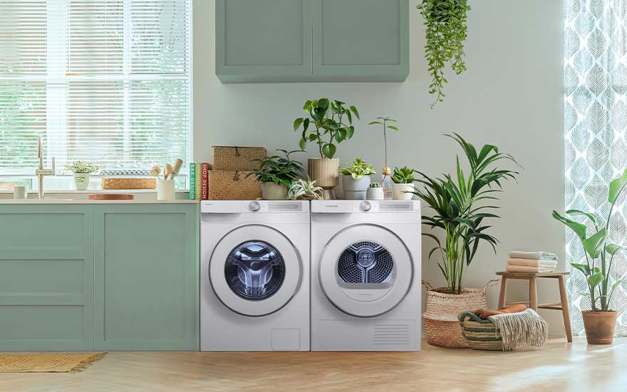 Frisgroene, lichte wasruimte met wasmachine en droger van Samsung, omringd door veel plantenpotten en manden, naast een groot raam.